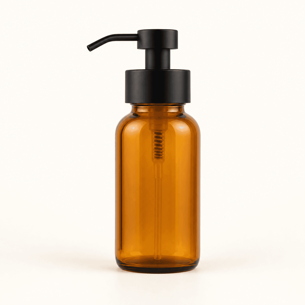 Amber glass soap dispenser with a matte black pump on a warm white background